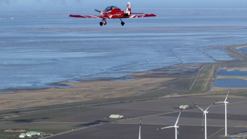 Rotes Sportflugzeug absolviert Testflug über Windpark