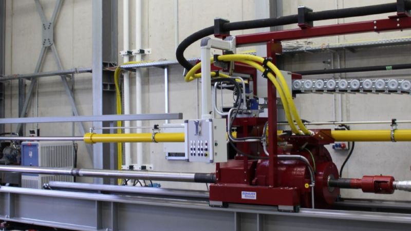 Output configuration of the test rig. The tests are being carried out with a horizontally mounted drilling rig. The drive (red, in the middle of the picture) drives the drill pipe, which protrudes from the hall onto the test site.