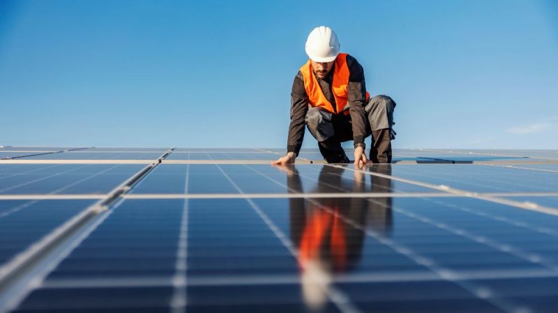 Symbolfoto eines Handwerkers bei der Installation von Solarzellen auf einem Dach.