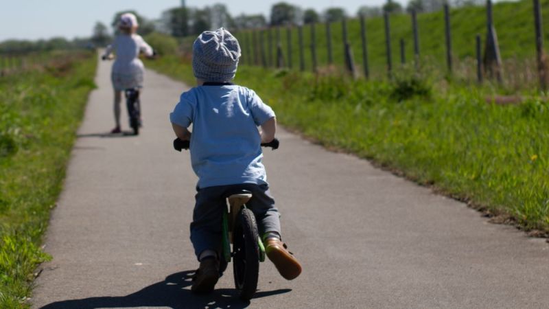 Symbolfoto: Kinder fahren auf Fahrrädern in Richtung Windenergieanlagen.