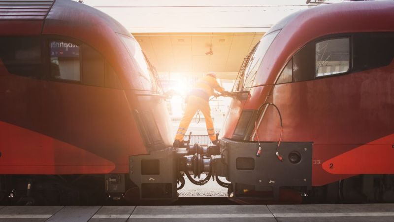 Symbolfoto: Ein Ingenieur koppelt zwei Bahnwaggons aneinander.