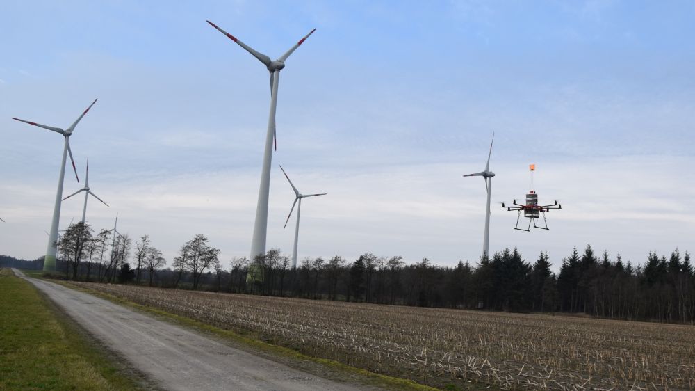 Das Foto zeigt einen Oktokopter vor Windenergieanlagen im Binnenland