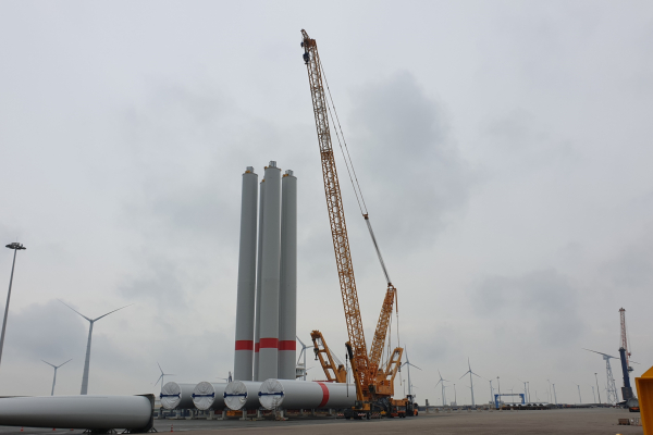 Four towers of wind turbines stand next to each other in the port, next to a yellow crane.