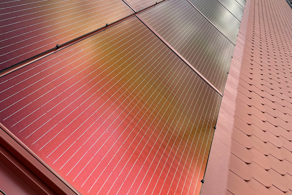 Close-up of the roof integration of brick-red photovoltaic modules.